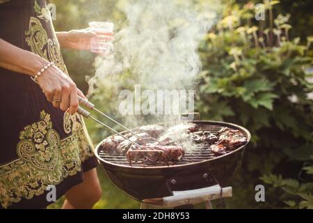 Mittelteil der Frau Grillen Fleisch auf Grill im Hinterhof Stockfoto