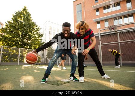 Männliche Freunde mit Basketball spielen im Sportplatz Stockfoto