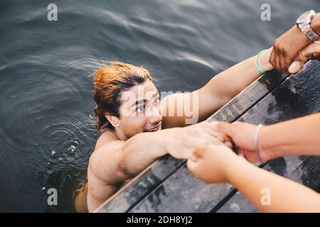 Zugeschnittenes Bild von männlichen Freunden, die Hände mit jungen Mann halten Im See Stockfoto
