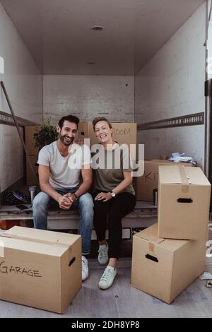 Portrait von lächelnden männlichen und weiblichen Partnern, die an Pappe sitzen Boxen im Lieferwagen Stockfoto