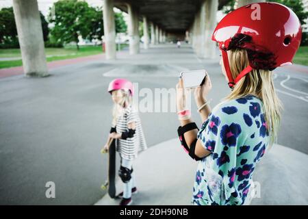 Mädchen fotografieren Freund durch Smartphone im Skateboard Park Stockfoto