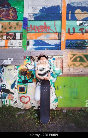 Portrait eines lächelnden Mädchens, das mit Skateboard gegen die Graffiti-Wand steht Stockfoto