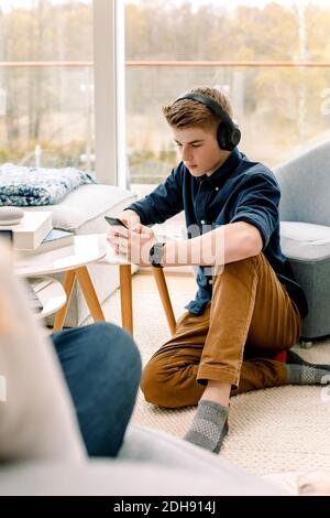 Teenager, der zu Hause auf dem Boden sitzt, mit dem Mobiltelefon Stockfoto