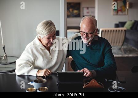 Lächelndes Seniorenpaar mit digitalem Tablet beim Essen Tisch im Wohnzimmer Stockfoto