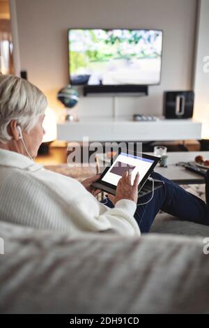 Ältere Frau mit digitalem Tablet, während sie auf dem Sofa sitzt Wohnzimmer Stockfoto