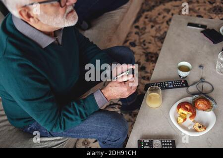 High-Angle-Ansicht des älteren Mannes mit Smartphone während Sitzen auf einem Sofa im Wohnzimmer Stockfoto