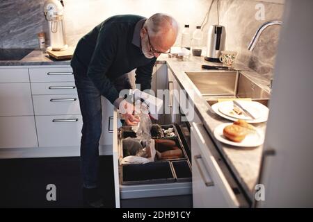 Älterer Mann, der zu Hause die ausgepackte Kiste in den Mülleimer wirft Stockfoto