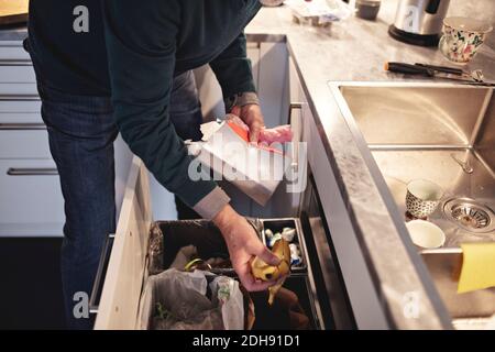 Mittelteil eines älteren Mannes, der zu Hause Müll in den Mülleimer wirft Stockfoto