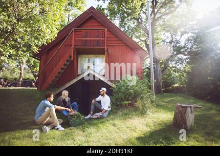 Freunde sitzen mit Gemüsekiste außerhalb der Hütte an sonnigen Tag Stockfoto