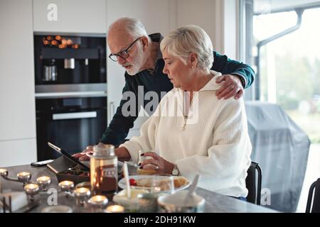 Ältere Paare, die beim Essen auf ein digitales Tablet schauen Tisch im Wohnzimmer Stockfoto