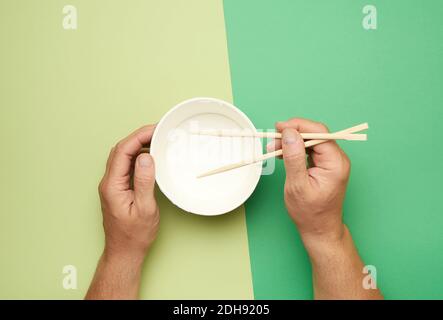 Paar Holzstäbchen in einer männlichen Hand und leer Papierplatte Stockfoto