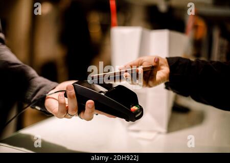 Kurze Hand der weiblichen Kundin, die im Geschäft telefonisch bezahlt hat Stockfoto