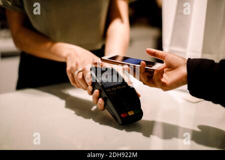 Kleine Hand von jungen Kunden, die über das Mobiltelefon bezahlen Modegeschäft Stockfoto
