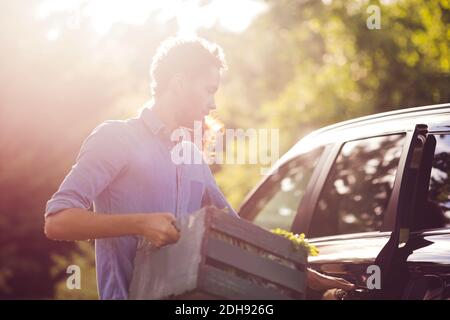 Mann, der die Autotür öffnete, während er die Holzkiste bei Sonnenschein hielt Tag Stockfoto