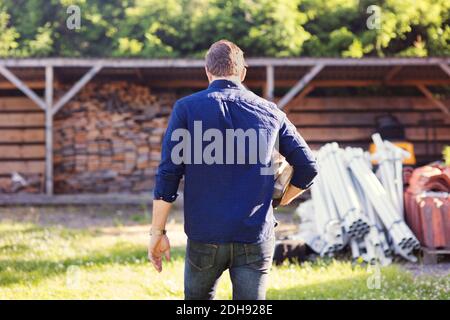 Rückansicht des Mannes, der Feuerholz trägt, während er zum Schuppen geht Stockfoto