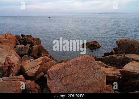 Blick auf rosa Granitsteine und Boote im Wasser in Mount Desert Island, Maine, USA, in der Nähe der Bass Harbor Head Light Stockfoto