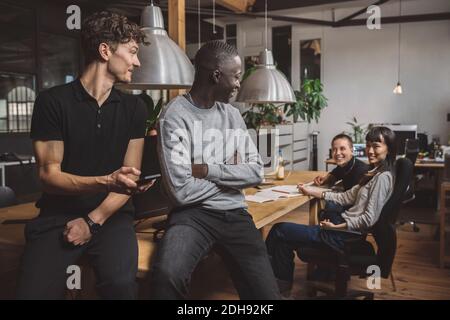 Lächelnde Geschäftsleute im Gespräch mit weiblichen Kollegen am Arbeitsplatz Stockfoto
