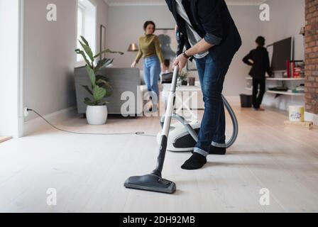 Niedriger Abschnitt des Mannes, der Boden mit Frau und Sohn saugt Im Wohnzimmer Stockfoto