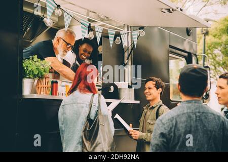 Besitzer mit Assistent im Gespräch mit lächelnden Kunden von Food Truck Stockfoto