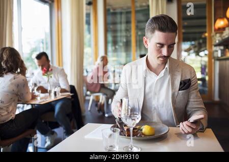 Geschäftsmann, der Mittagessen isst, während er Smartphone im Restaurant benutzt Stockfoto