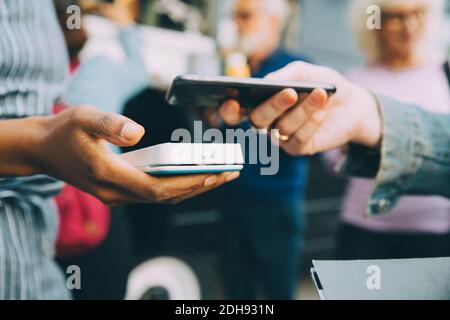 Die Hand des Kunden, der in der Stadt über ein Smartphone bezahlt, ist abgeschnitten Stockfoto