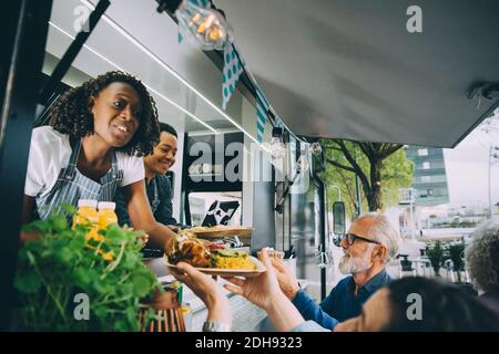 Lächelnde Besitzer, die den Gästen während des Stehens indisches Essen geben Gewerbliches Landfahrzeug Stockfoto