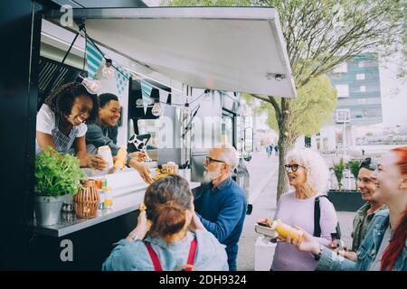 Lächelnde männliche und weibliche Kunden, die mit den Besitzern von Food-Trucks sprechen In der Stadt Stockfoto