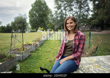 Porträt von lächelnden mittleren Erwachsenen Frau sitzt auf Holz in Gemüsegarten Stockfoto