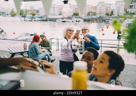Lächelnder älterer Mann und Frau, die Selfie unter den Kunden machen Foodtruck Stockfoto