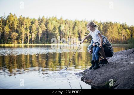 Vater hält Tochter während des Fischens beim Crouching am See Stockfoto