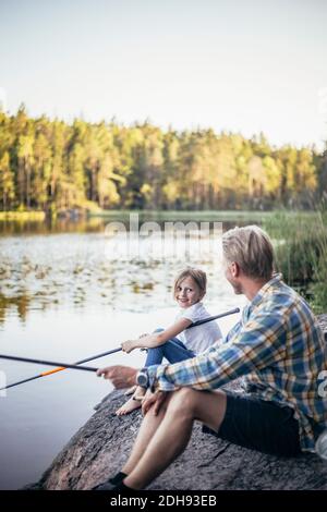 Lächelnde Tochter, die Vater ansieht, während sie am See angeln Stockfoto