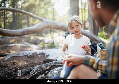Tochter, die Wassermelone isst, während sie Vater im Wald ansieht Stockfoto