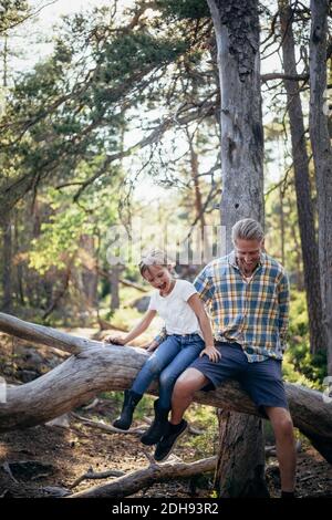 Glücklicher Vater und Tochter, die sich auf einem umgestürzten Baum einziehen Wald Stockfoto