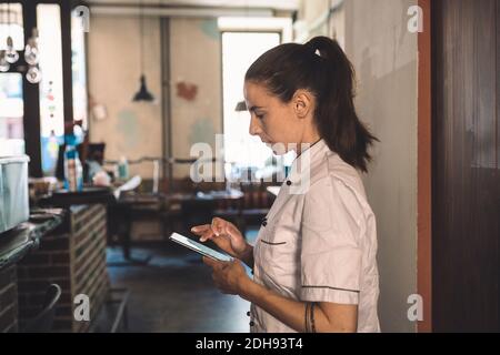 Seitenansicht der Köchin mit Smartphone im Restaurant Stockfoto