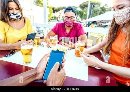 Milenial Freunde mit geschlossenen Gesichtsmasken mit Tracking-App mit Mobile Smartphones - Neue normale Lifestyle-Konzept von gelangweilten jungen Menschen in der Brauerei Bar Stockfoto
