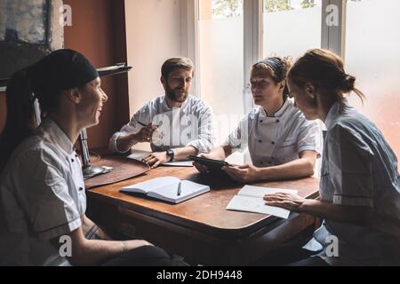 Männliche und weibliche Köche diskutieren während sie am Tisch sitzen Restaurant Stockfoto