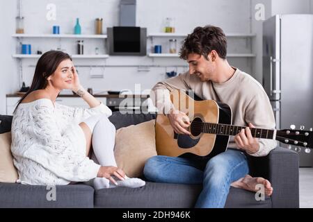 Lächelnde Frau sitzt neben Freund spielen akustische Gitarre zu Hause Stockfoto