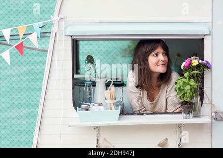 Nachdenkliche weibliche Besitzerin, die durch das Fenster des Food-Trucks schaut Stockfoto