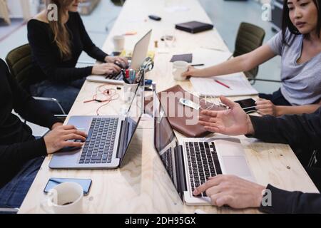 Zugeschnittenes Bild von vier Personen, die am Schreibtisch im Büro einen Laptop verwenden Stockfoto