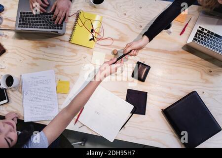 Direkt über der Aufnahme der Frau, die Stift an Kollegen gibt Holzschreibtisch Stockfoto