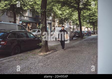 Delivery Mann mit Paket beim Gehen am Straßenrand in der Stadt Stockfoto