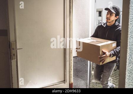 Selbstbewusster Lieferer mit Paket vor der Haustür Stockfoto