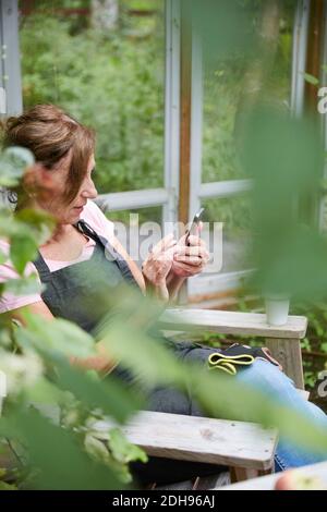 Gärtnerin mit Handy, während sie im Hof sitzt Stockfoto