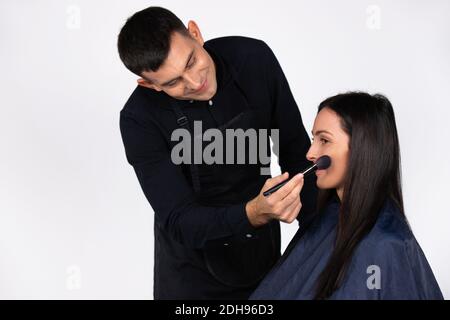 Cool männlichen Make-up Künstler tun Make-up zu jungen Geschäftsfrau. Schönheit, Mode und Geschlechterstereotypen auf Weiß. Stockfoto