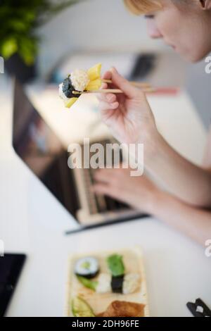 High-Angle-Ansicht der Geschäftsfrau mit Sushi während der Verwendung Laptop Am Tisch im Büro Stockfoto