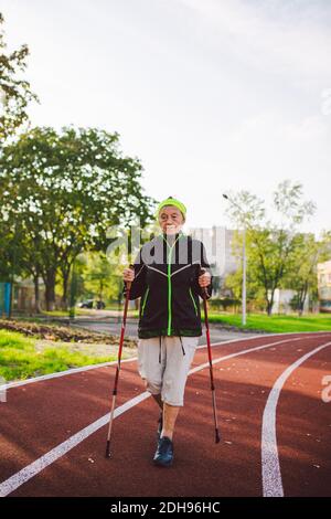 Ältere Frau, die mit Wanderstöcken im Stadion auf einer roten Gummihülle läuft. Ältere Frau 88 Jahre alt macht Nordic Walking exerci Stockfoto