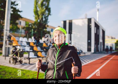 Aktive ältere kaukasische ältere Frauen von 90 Jahren üben Nordic Walking mit Skistöcken auf einer Strecke mit roter Gummibeschichtung. Stockfoto