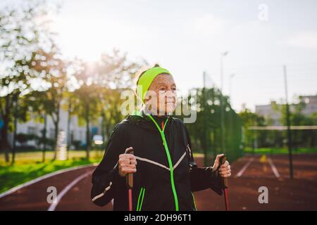 Aktive ältere kaukasische ältere Frauen von 90 Jahren üben Nordic Walking mit Skistöcken auf einer Strecke mit roter Gummibeschichtung. Stockfoto