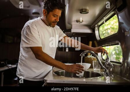 Mann füllt Trinkwasser durch Wasserhahn in Wohnmobil Anhänger Stockfoto