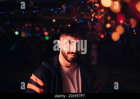 Porträt von lächelnden bärtigen Mann gegen beleuchtete bunte Lichter an Bar Stockfoto